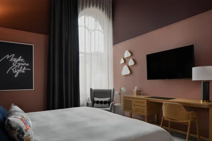 Boutique hotel room with desk, TV, painting, and king sized bed.