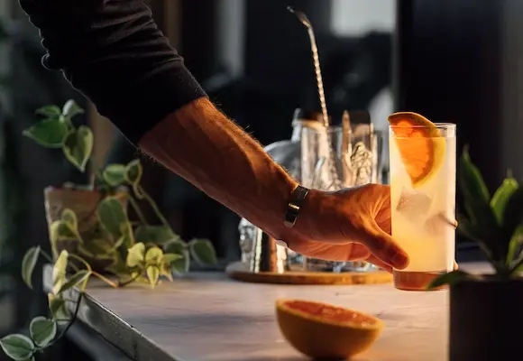 Bartender wearing a black sweater serving a beautiful paloma to a customer